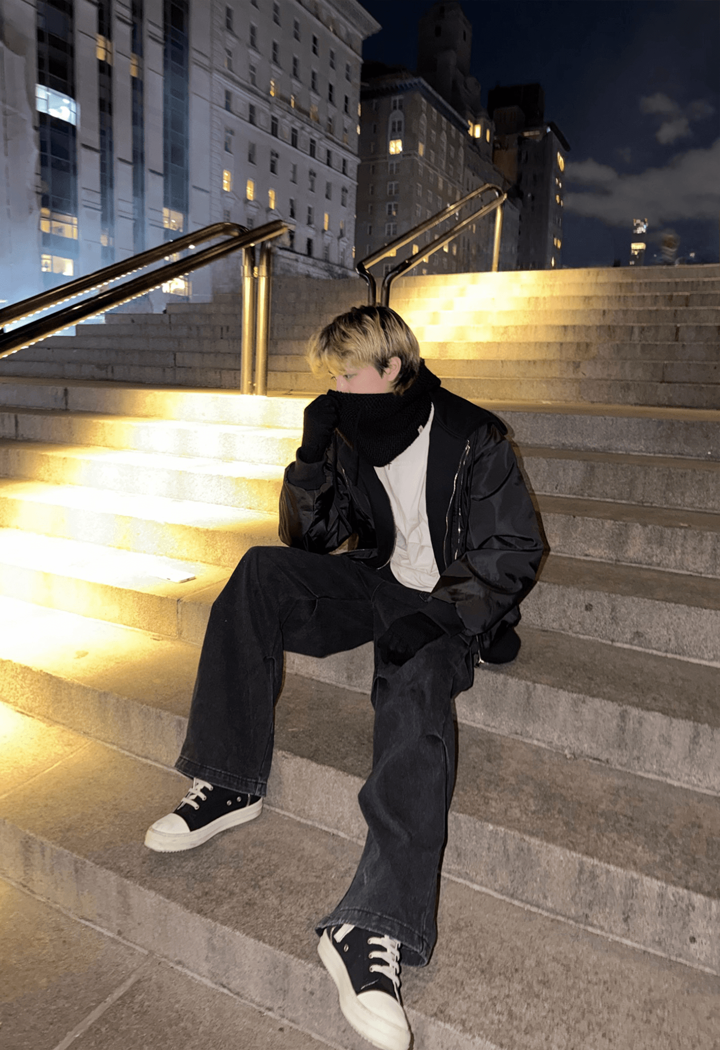 Devin Widmer sitting on the Met museum steps at night, NYC skyline behind